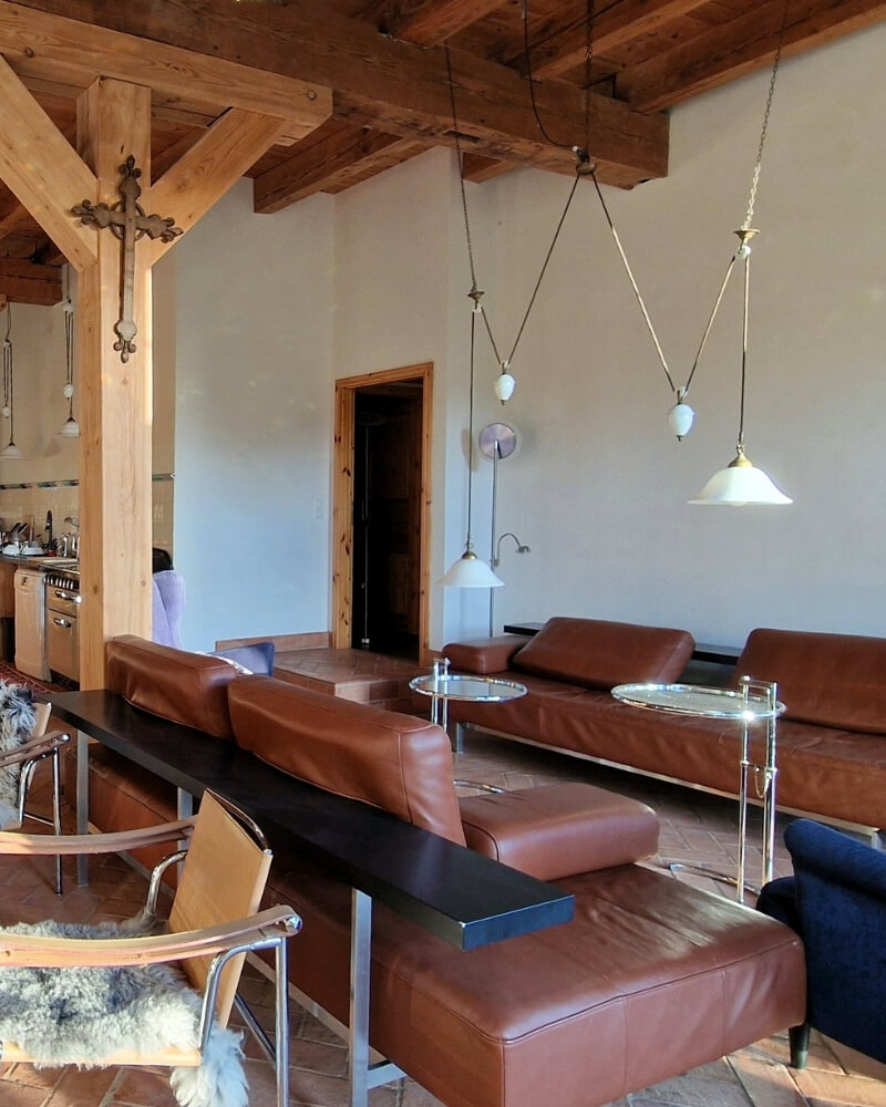 Wohnbereich im Scheunenloft Usedom mit braunen Ledersofas, Holzbalken und stilvollen Hängeleuchten
